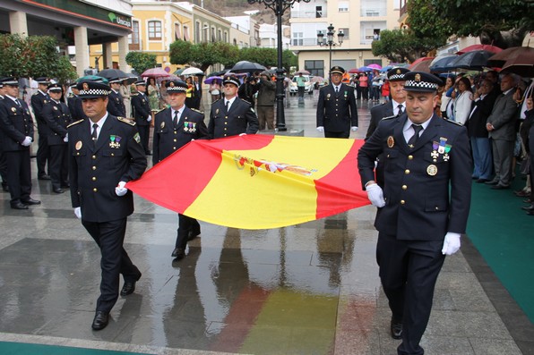 Agentes de la Policia Local portan la bandera nacional que se ha izado en el mastil del monumento que preside la Plaza de la Constitución
